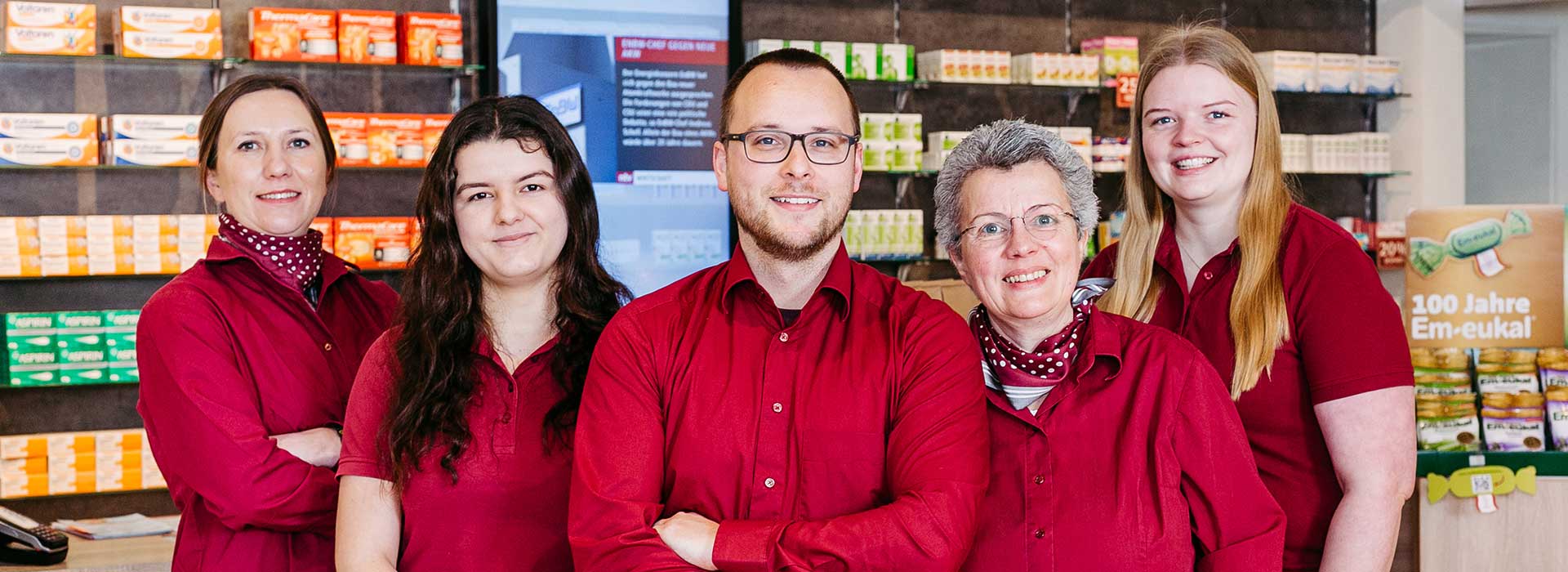 Fünf Mitarbeiter in roter Kleidung vor den Verkaufsregalen in der Apotheke