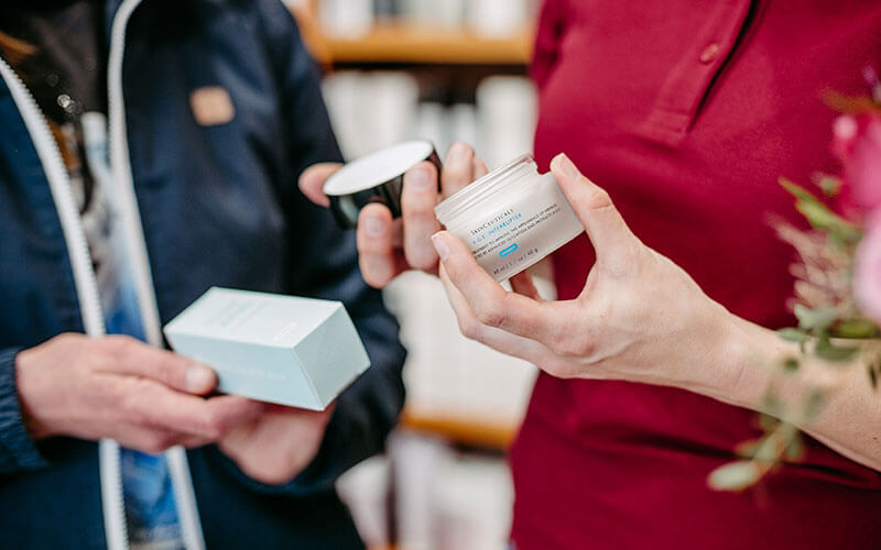 Die Hände einer Apothekerin und eines Kunden, die Cremes halten.